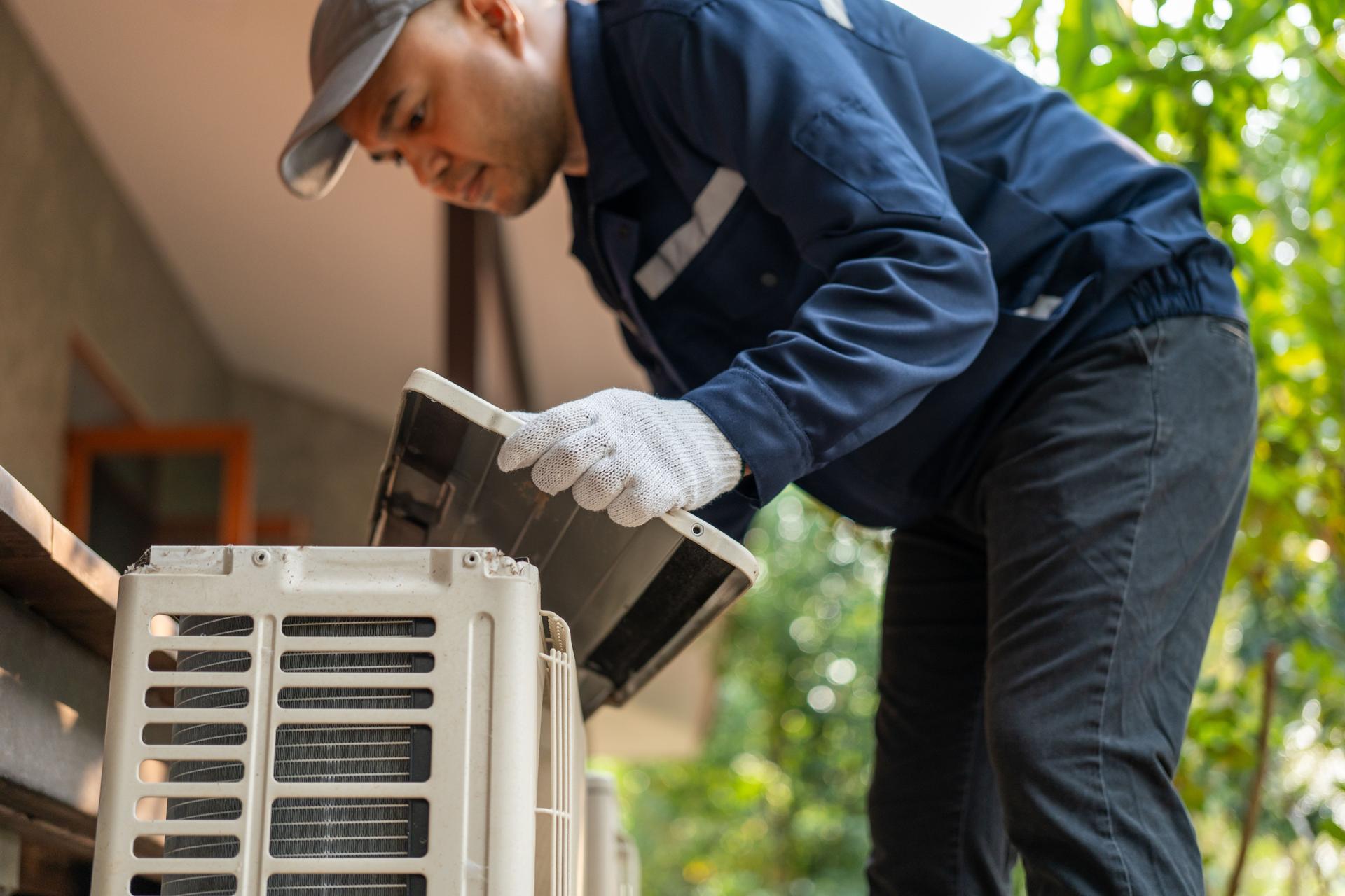 Air conditioner service outdoor checking fix repair. Air conditioner cleaning technician He opened the front cover and took out the filters and washed it. He in uniform wearing rubber